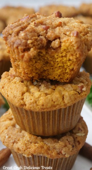 Three muffins stacked on top of each other and the top muffin has a bite taken out of it.