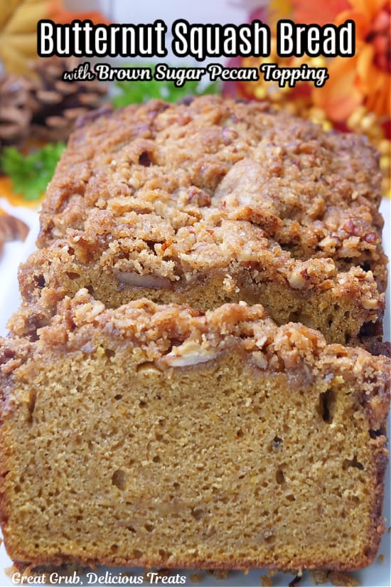 A loaf of butternut squash quick bread with a crunchy topping, sliced and has fall foliage in the background.