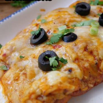 A white plate with blue trim with two ground beef enchiladas on it with sliced black olive and cilantro on top.