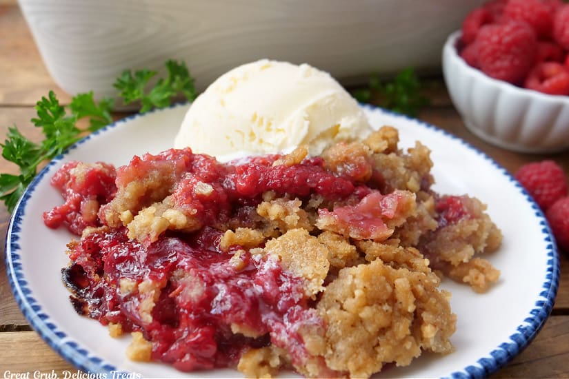 A horizontal photo of raspberry crumble with a scoop of vanilla ice cream.