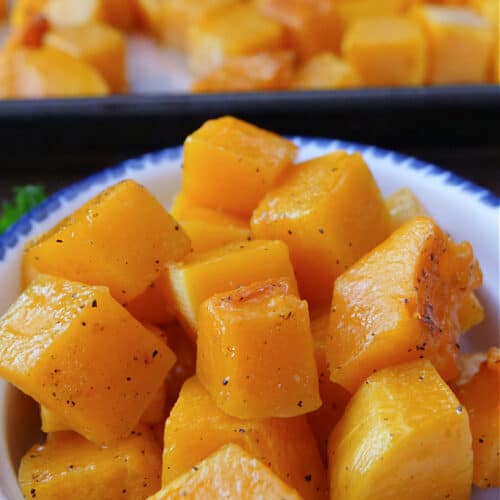 A white bowl with blue trim filled with a serving of roasted butternut squash cubes.