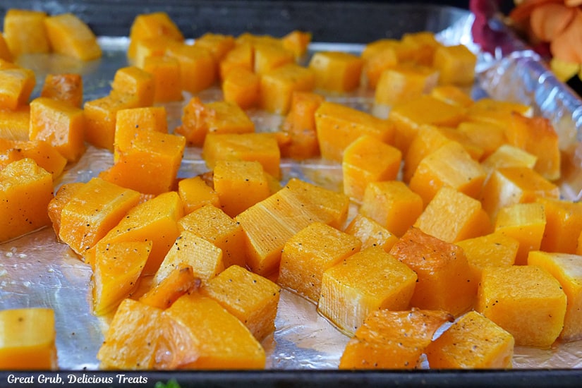 A baking sheet with aluminum foil on it with roasted butternut squash cubes after being oven roasted.