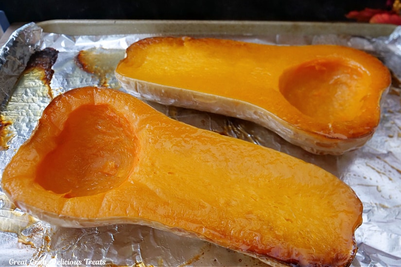 Two halves of roasted butternut squash on a baking sheet lined with foil after being pulled out of the oven.