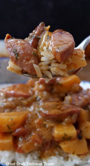 A close up of a bite of smoked sausage and potatoes on a fork with rice.