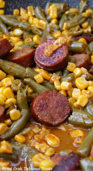 A close up of cooked sliced sausage, green beans and corn is a skillet.
