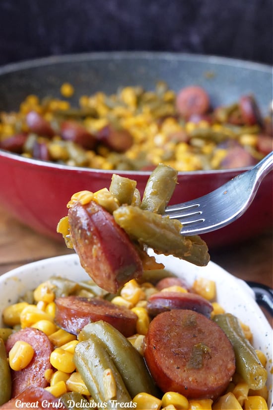 A bite of smoked sausage, green beans and corn on a fork.