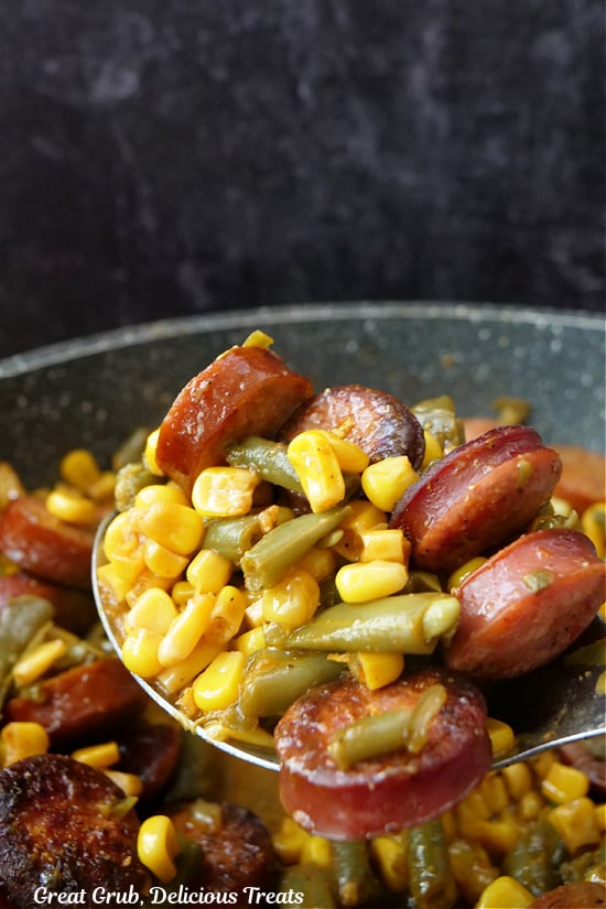 A large spoonful of sausage green beans and corn being scooped out of the skillet to be served.