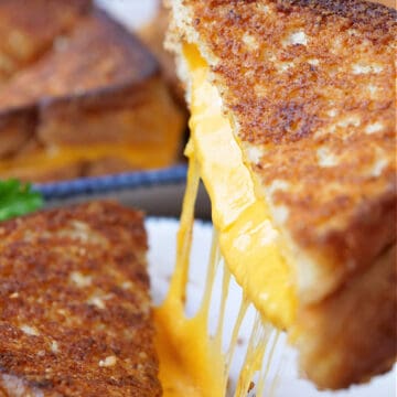 A half of a grilled cheese sandwich being lifted up off the plate showing all the cheesy goodness.