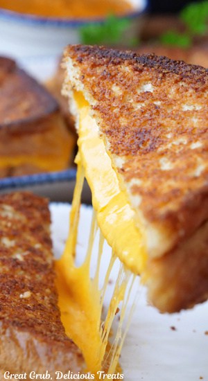 A half of grilled cheese being lifted from the plate showing the melted cheese.