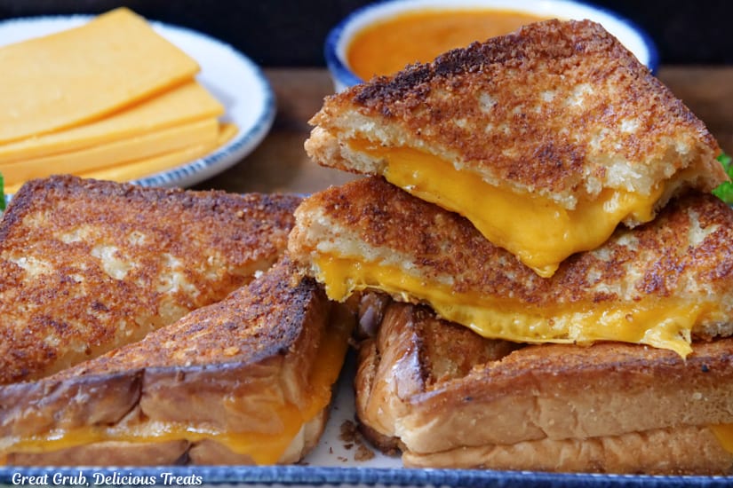 A horizontal photo of three Parmesan crusted grilled cheese sandwiches on a rectangle plate with blue trim.