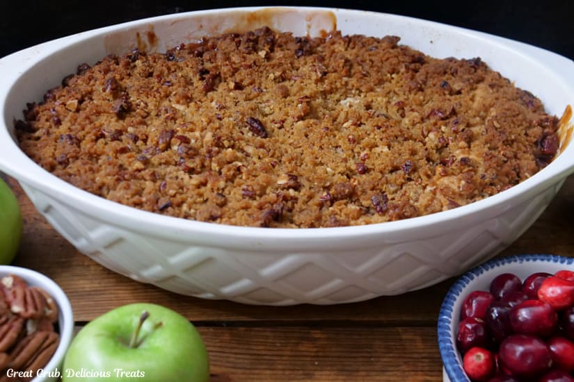 A horizontal photo of a white ovel baking dish filled with apple cranberry cobbler right after being pulled out of the oven.