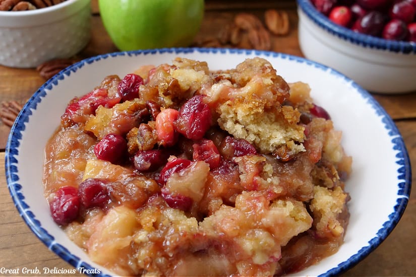 A horizontal photo of a white bowl with blue trim filled with a serving of apple cranberry cobbler.