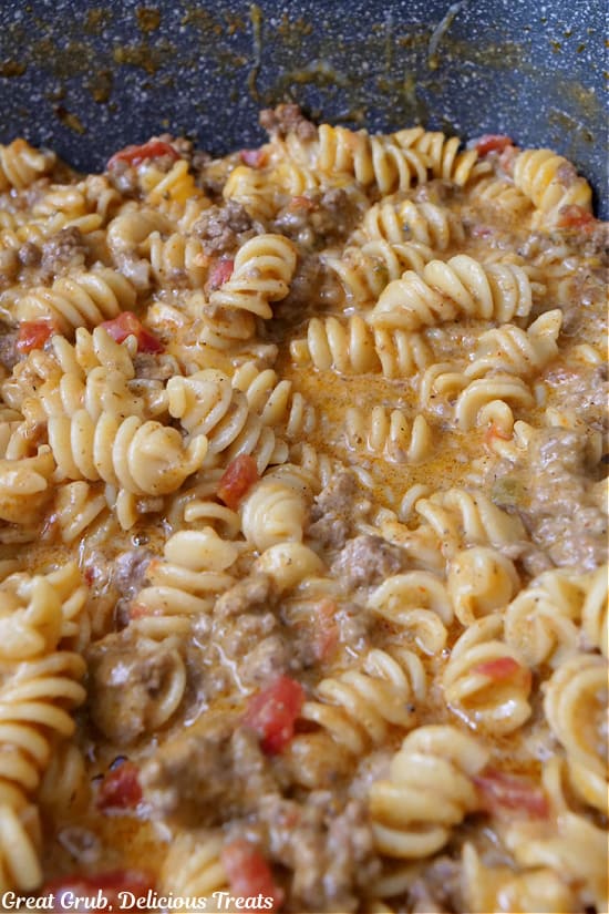 A pot with ground beef, rotini pasta, diced tomatoes, and cheese in a creamy sauce.