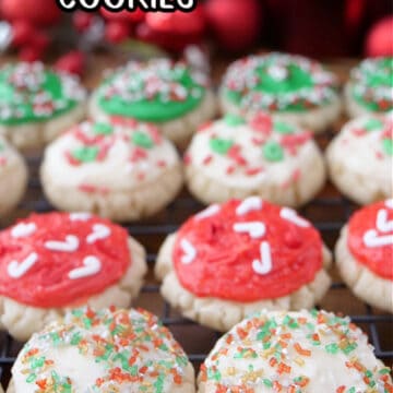 A wire rack with mini Christmas cookies on it that are decorated with red, green and white frosting, and festive sprinkles on top.