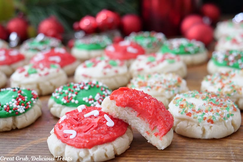 A horizontal photo of a bunch of mini Christmas cookies on a wood surface with red, green, and white frosting and each cookie is sprinkled with festive sprinkles.