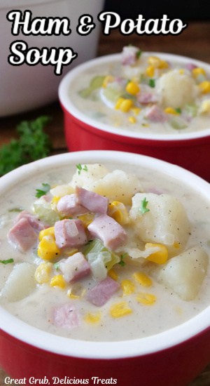 A close up of two red soup bowls filled with potatoes, ham, corn, in a creamy base.