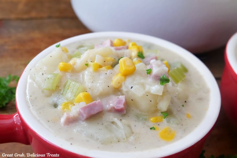 A close up of a red and white bowl filled with ham and potato soup.