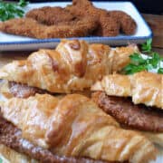 A white plate with three croissant fried chicken sandwiches topped with honey butter.