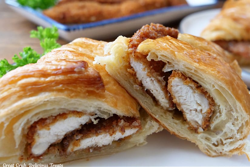 A horizontal photo of a croissant sandwich filled with fried chicken strips with honey butter.