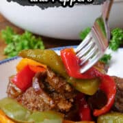 A white bowl with blue trim with a serving of Italian sausage and peppers in it with a fork digging in to grab a bite.