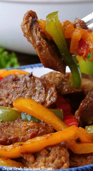 A close up of a fork with sausage slices and strips of bell pepper on it.