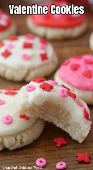 A close up of a few sugar cookies decorated with white, pink and red frosting and candy sprinkles on top.