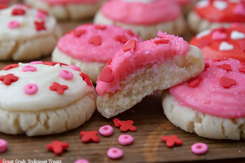 A horizontal photo of bite-size sugar cookies with white, pink and red buttercream frosting on top along with candy sprinkles.