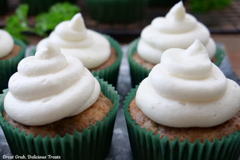 A horizontal photo of four muffins with cream cheese frosting on top placed on a silver plate.
