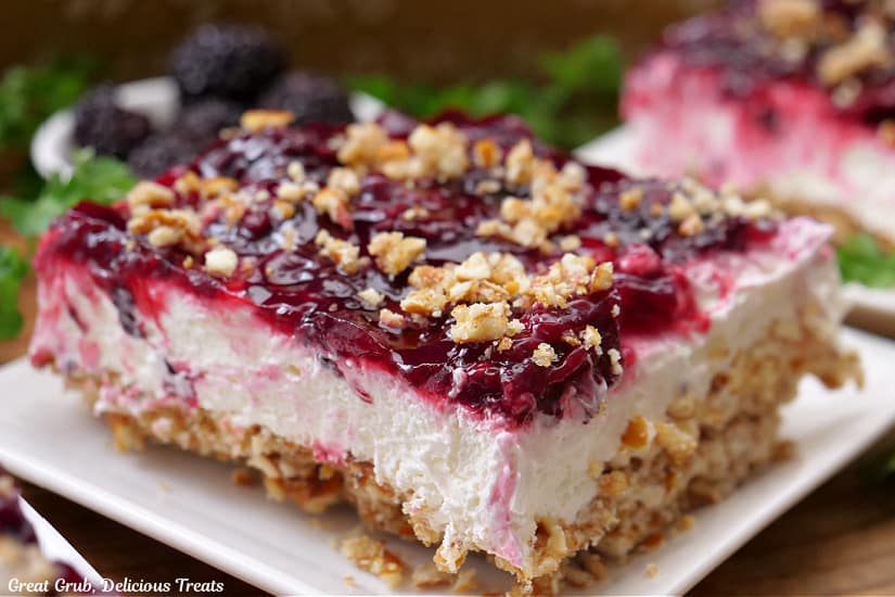 A horizontal photo of a white plate with a serving of blackberry pretzel dessert on it.
