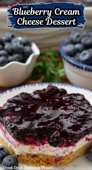 A white plate with blue trim with a serving of blueberry cream cheese dessert on it.