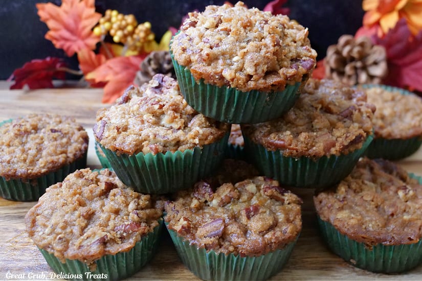 A horizontal photo of about 8 muffins of a wood surface with fall leaves in the background.