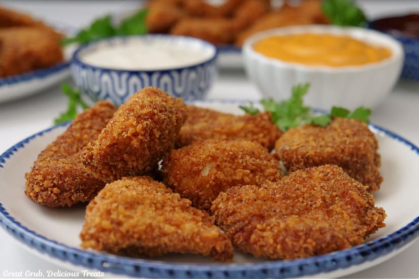 A horizontal photo of a white plate with blue trim filled with chicken nuggets with two small bowls with dipping sauce in them.