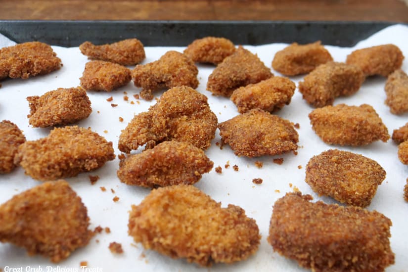 A baking sheet lined with paper towels with deep fried chicken nuggets on it.