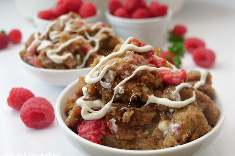 A horizontal photo of cinnamon bread pudding with fresh raspberries and a white chocolate drizzle over the top.