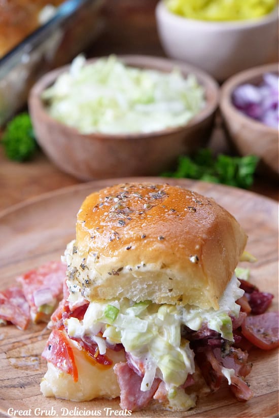 One Italian slider on a round wood plate showing the chopped cold cuts, the lettuce mixture, and the seasoned butter mixture on top.