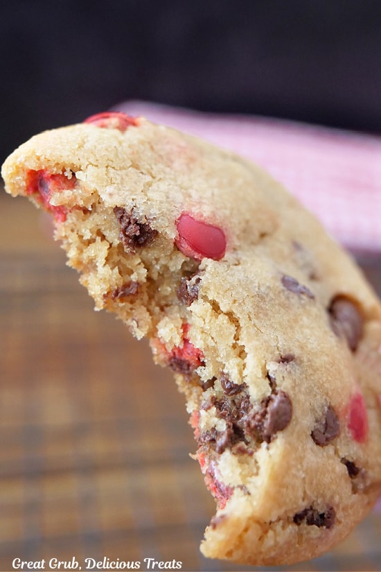 A super close up photo of a M&M chocolate chip cookie with a bite taken out of it.