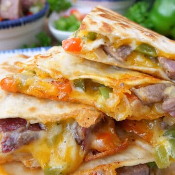 A stack of pieces of steak quesadilla placed on top of each other showing all the cheese and ingredients.