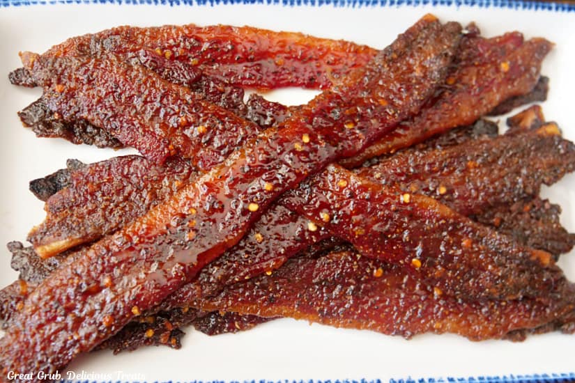 A horizontal photo of a white rectangle plate with blue trim filled with about 8 pieces of candy bacon on it.