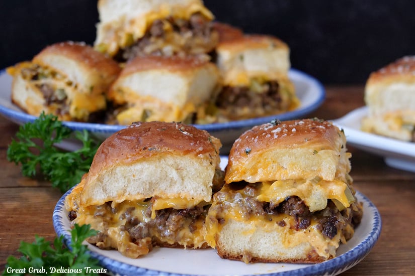 A horizontal photo of cheeseburger sliders on white plates with blue trim.