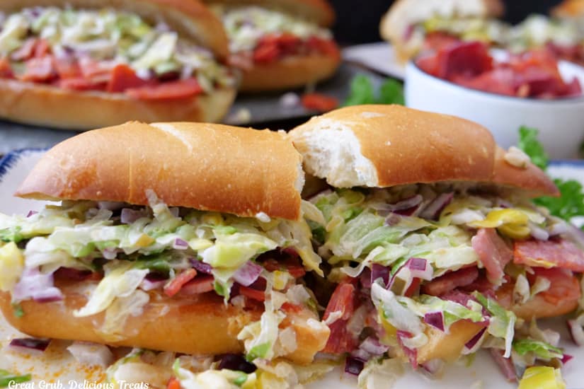 A horizontal photo of a chopped Italian sandwich cut in half on a white plate with more sandwiches in the background.