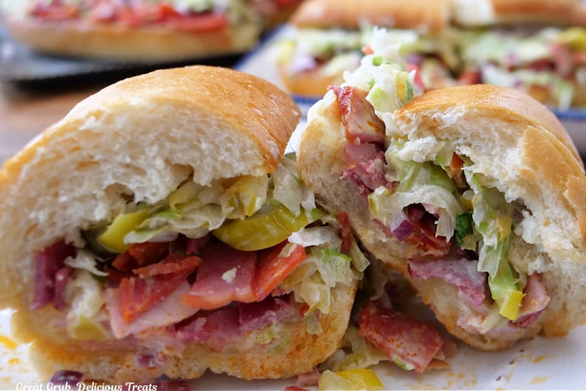 A close up of a hoagie sandwich cut in half and placed on a white plate.