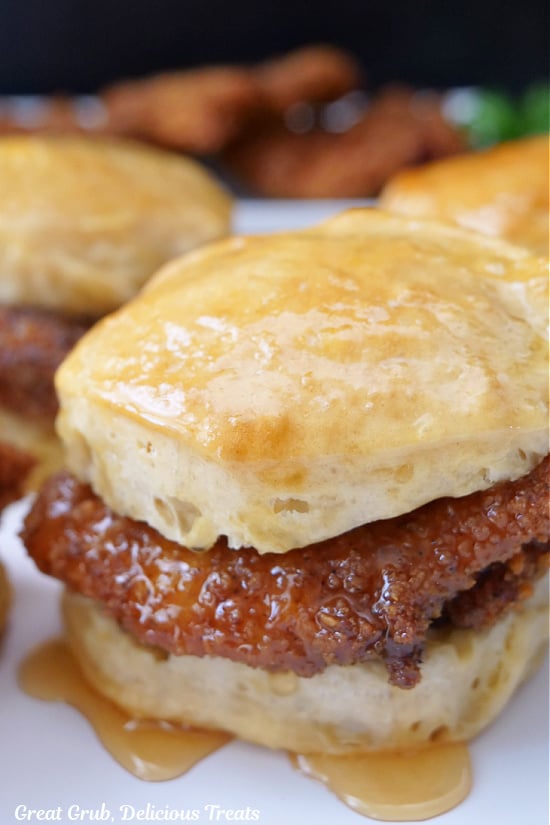A close up of a buttermilk biscuit with a honey butter smothered fried chicken breasts nestled in between.