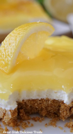 A close up of a slice of lemon dessert with a lemon slice on top with a bite taken out of it.