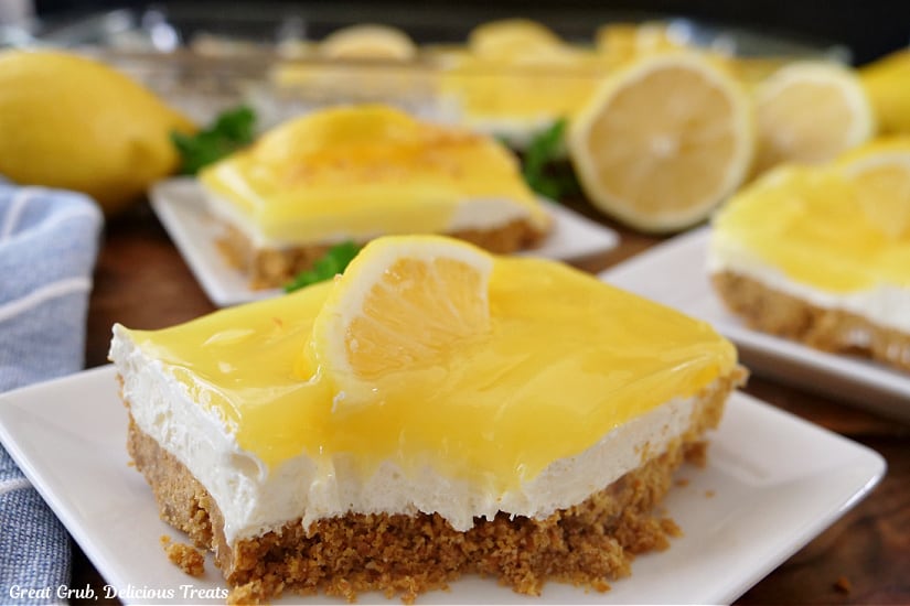 A horizontal photo of three small square white plates with a slice of lemon dessert on each plate.