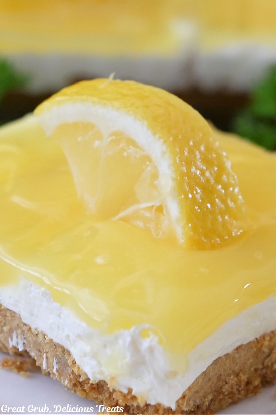 A close up of a slice of a lemon layered dessert with a graham cracker crust, a cream cheese layer, and topped with lemon pie filling.