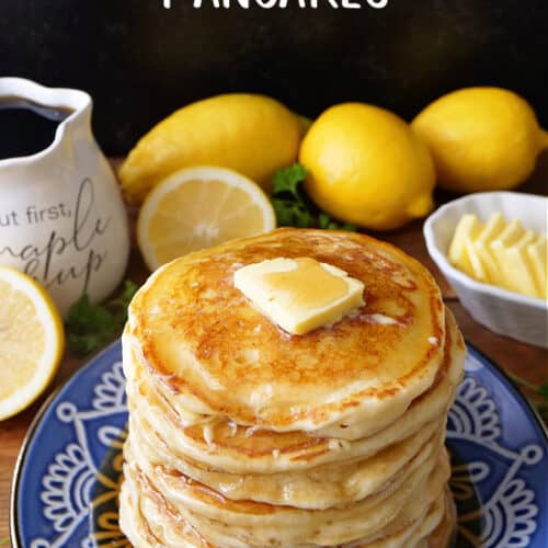 A blue plate with a stack of lemon ricotta pancakes on it with fresh lemons, butter, and syrup in the background.