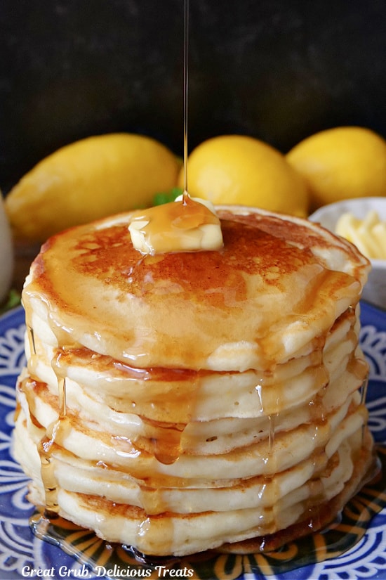 A stack of pancakes with a pad of butter on top with syrup being drizzled over the top.