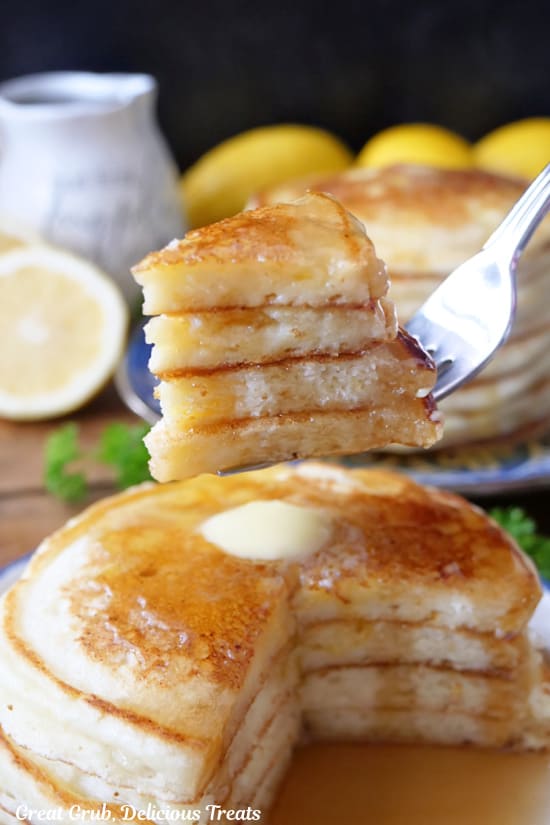 A bite of pancakes on a fork held above a stack of pancakes.