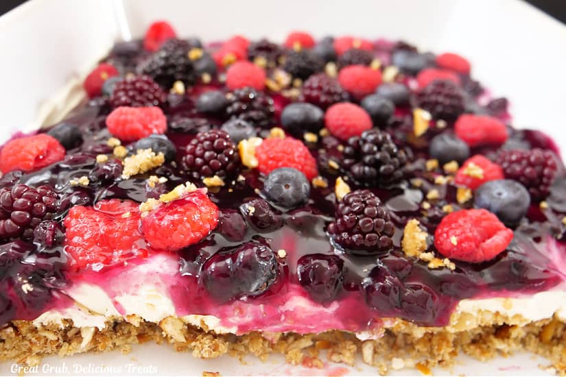 A white baking dish filled with a pretzel dessert topped with cream cheese and mixed berries.