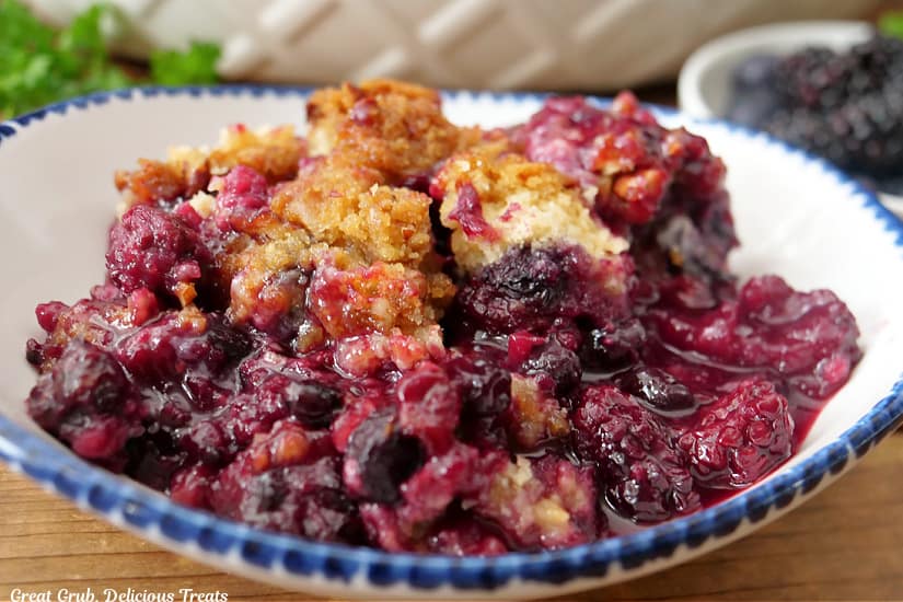 A horizontal photo of a white bowl with blue trim filled with a serving of berry cobbler.